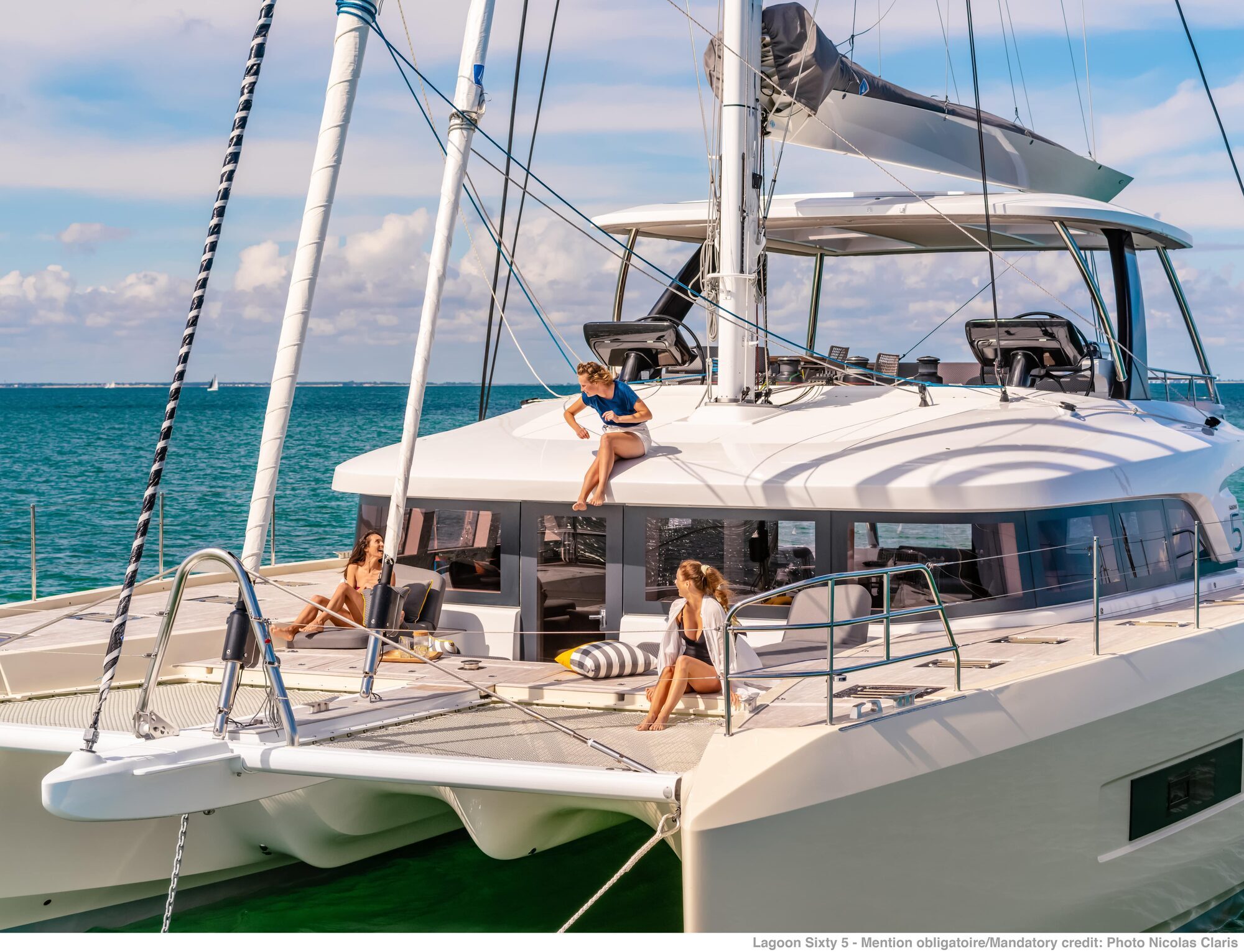 Lagoon 65 luxury sailing catamaran anchored at sea with guests relaxing on the foredeck Lagoon 65 luxury sailing catamaran anchored at sea with guests relaxing on the foredeck